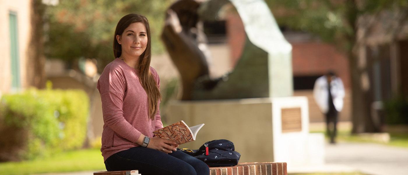 英语 student reading a book outside on campus courtyard